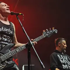 Dwóch muzyków Acid Drinkers grających na gitarach basowych na scenie.