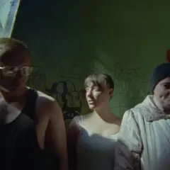 Trzy osoby stoją przed ścianą z graffiti.