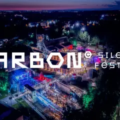 Nocne, oświetlone miasto i teren festiwalowy. Wielkie litery "CARBON Silesia Festival" na pierwszym planie.