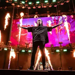 Wokalista Falling in Reverse na scenie z płomieniami i ekranem w tle.