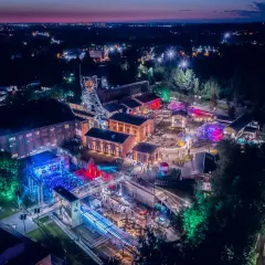 Nocny festiwal z kolorowymi światłami na terenie postindustrialnym. Ludzie bawią się na koncertach i stoiskach. To świetne miejsce na **carbon festival**!