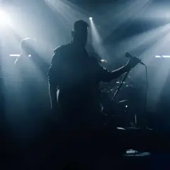 Zespół muzyczny na scenie, wokalista z mikrofonem, saksofonista, światła sceniczne.