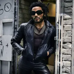 Lenny Kravitz w skórzanej kurtce i okularach, oparty o drzwi z graffiti, jakby właśnie wysiadł z łodzi.