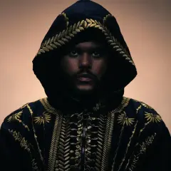 The Weeknd w czarnej, haftowanej złotem kurtce z kapturem, patrzący prosto w obiektyw.