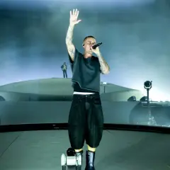 Justin Bieber śpiewa na scenie z podniesioną ręką, otoczony mgłą i światłami.
