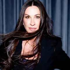 Alanis Morissette z rozwianymi włosami, w czarnej marynarce, gotowa na koncert.