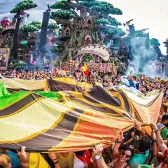 Tłum ludzi na festiwalu Tomorrowland, trzymający kolorową flagę, z imponującą sceną w tle.