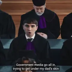Młody mężczyzna w todze sądowej przemawia przed grupą sędziów w togach.