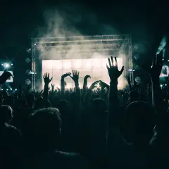 Tłum ludzi z podniesionymi rękami na koncercie przed sceną oświetloną światłami i dymem.