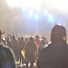 Tłum ludzi na festiwalu w deszczu, widok na scenę z oświetleniem.