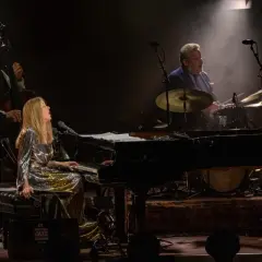 Diana Krall koncert: wokalistka i pianistka w błyszczącej sukni, kontrabasista i perkusista tworzą magiczną atmosferę jazzowego wieczoru.