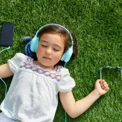 Dziewczynka w słuchawkach leży na trawie obok telefonu i okularów.
