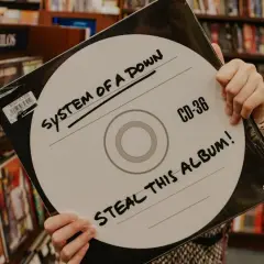 Ręce trzymają okładkę płyty System of a Down "Steal This Album!". Wybór między winylami a CD.