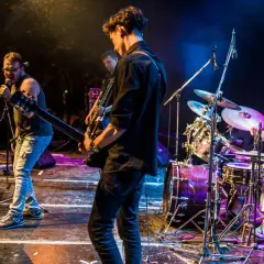 Zespół grający na żywo, wokalista śpiewa do mikrofonu, gitarzyści na scenie, perkusista za zestawem. Klimat jak z najlepszych zespołów lat 80.