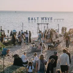 Ludzie na plaży podczas festiwalu Salt Wave, z napisem "SALT WAVE" nad wodą.