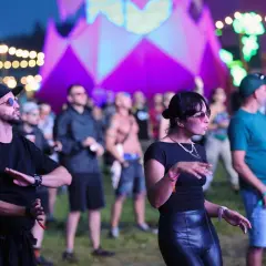 Ludzie tańczący na festiwalu Audioriver w Łodzi, z kolorową scenografią w tle.