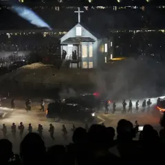 Scena z koncertu Donda 2: biały kościół z krzyżem na dachu, otoczony dymem, ludźmi i samochodami, w blasku reflektorów.