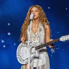 Shakira w Polsce na koncercie, śpiewa z białą gitarą i w białym stroju z frędzlami.