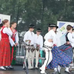 Grupa ludzi w tradycyjnych strojach ludowych tańczy na scenie.