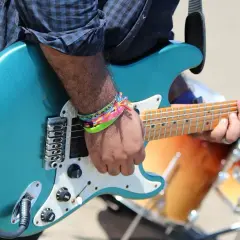 Muzyk grający na turkusowej gitarze elektrycznej, w tle bębny.