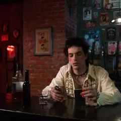 Młoda osoba z makijażem i biżuterią, siedząca przy barze, odzwierciedla ducha punk subkultury.