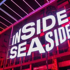 Jasne, oto opis alternatywny:

Duży neon "INSIDE SEASIDE" świeci białym światłem na tle czerwonej, nowoczesnej fasady budynku.