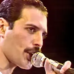 Freddie Mercury śpiewający do mikrofonu na scenie.