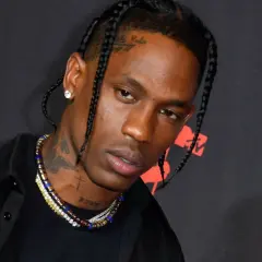 Travis Scott w czarnej koszuli i z warkoczami, z naszyjnikami i tatuażami na szyi.