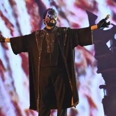 The Weeknd w czarnej, zdobionej masce i stroju, śpiewa na koncercie.
