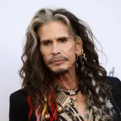 Steven Tyler z kolorowymi pasemkami we włosach, w czarnej marynarce i z biżuterią.