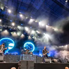 Zespół Bullet For My Valentine gra na scenie podczas koncertu, w tle niebieskie ekrany i światła.