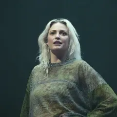 Emily Armstrong w siatkowej bluzce na ciemnym tle.