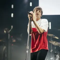 Louis Tomlinson śpiewa na koncercie w Polsce, w czerwono-białej koszulce, z zamkniętymi oczami.