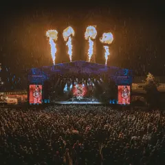 Koncert na Mystic Festival w deszczu, z płomieniami nad sceną i tłumem fanów.