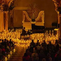 Pianista gra na fortepianie otoczony tysiącami świec, przed publicznością.