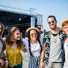 Pięć młodych osób w letnich stylizacjach pozuje do zdjęcia na tle sceny koncertowej.