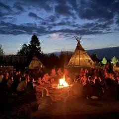 Ludzie siedzą przy ognisku pod namiotami tipi, tworząc atmosferę jednego z wielu festiwali na świecie.