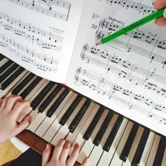 Dziecko uczy się gry na keyboardzie, ćwicząc nuty z podręcznika. Zielony ołówek zaznacza fragment do nauki.