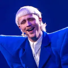 Joost Klein w niebieskiej marynarce, śpiewający na scenie z zamkniętymi oczami.
