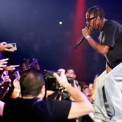 Travis Scott koncert: artysta śpiewa do mikrofonu, a fani z telefonami w dłoniach nagrywają występ.