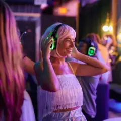 Kobieta w słuchawkach z podświetlanymi na zielono nausznikami tańczy na imprezie silent disco.