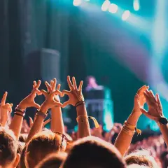 Tłum na letnim festiwalu, ręce w górze tworzą serca i gesty radości. Światła sceny tworzą magiczną atmosferę.