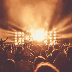 Tłum ludzi na festiwalu muzycznym, scena z jasnymi światłami i dymem.