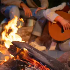 Przy ognisku siedzą ludzie, grają na gitarze i śpiewają piosenki na ognisko.