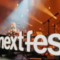Światła sceny oświetlają napis "next fest" i artystkę grającą na gitarze.