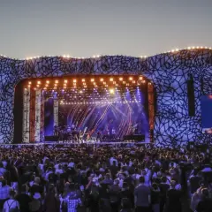 Tłum ludzi na koncercie w Warszawie. Na scenie artyści, a obok ekran z wokalistką.