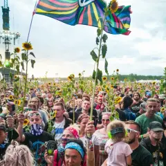 Tłum ludzi na festiwalu Pol'and'Rock trzymający słoneczniki i flagi, z widoczną sceną w tle.