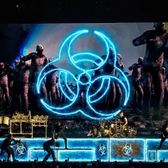 Koncertowy zespół na tle ekranu z symbolem biohazard i zombie.
