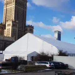 Biały namiot festiwalowy przed Pałacem Kultury w Warszawie, z nowoczesnymi wieżowcami w tle.