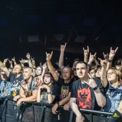 Tłum fanów na koncercie, wielu z nich pokazuje znak "rogi" rękami.